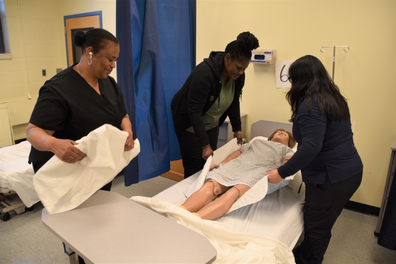 Students in ALI's Nursing Assistant program practice setting up a patient in bed during class.