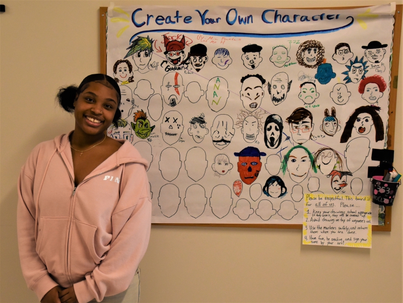 Resilience Academy's Mia Fountain stands outside the "Create Your Own Character" board she created with Art Teacher Michael Hollick.