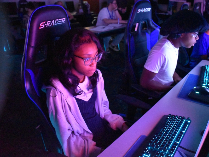 A student sits in a gaming chair in front of a computer during an esports competition.