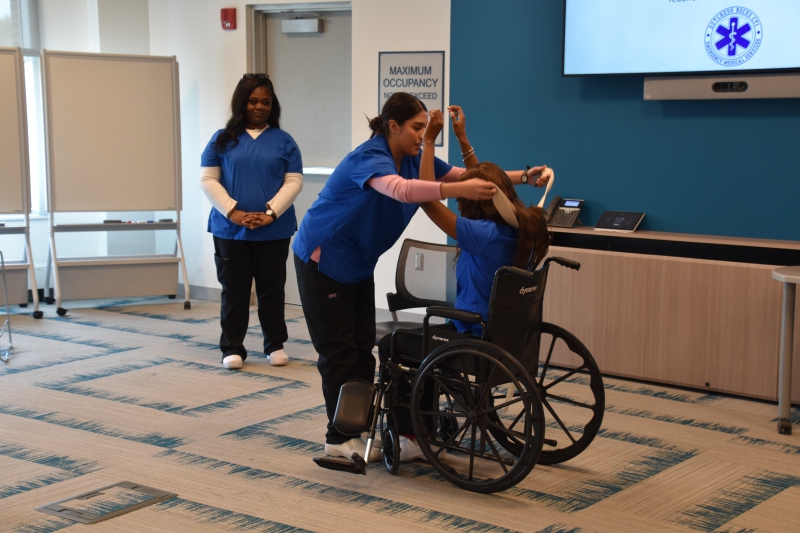 Nursing students demonstrate how to get a patient into a wheelchair using a transfer belt.