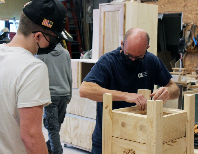 A construction trade student works with Teacher Thomas Skean on a planter.