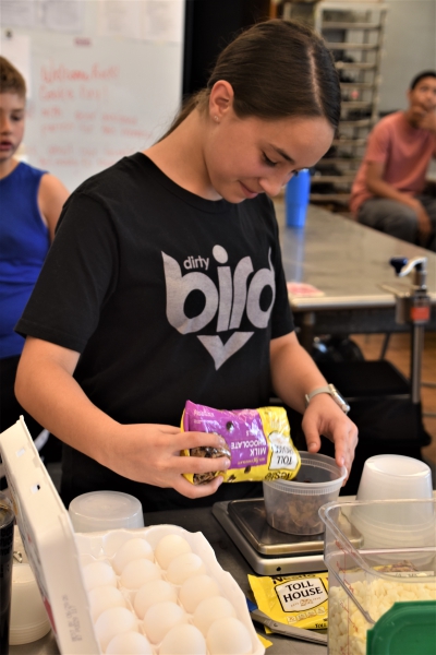 A student in the culinary class at the Middle School Summer CTI Experience pours chocolate chips in a container to make homemade cookies.