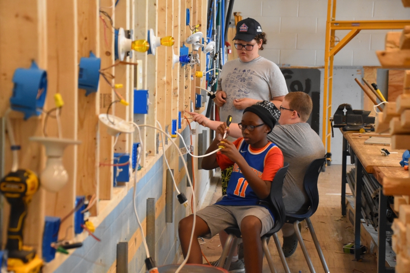 In the trade electric class at the Middle School Summer CTI Experience, middle school students are seen setting up wires and installing plugs.