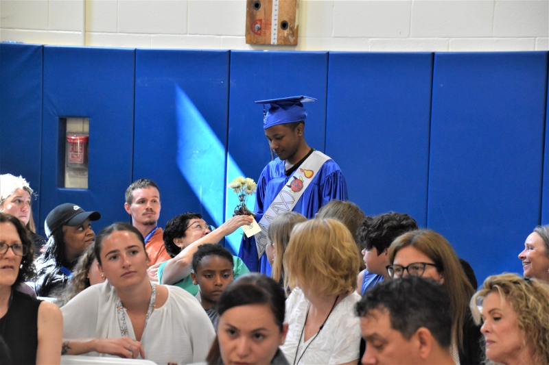 A student hands a flower to a staff member who helped them grow and reach the milestone of moving on to high school.