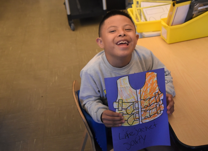 A student smiles and shows off his colorful life jacket in yellow and orange.